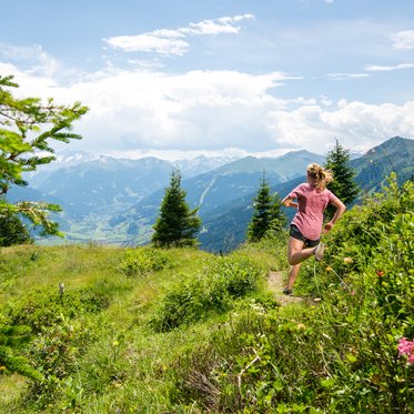 Trailrunner*in läuft auf einem alpinen Höhenweg mit Aussicht auf die Alpen im Gasteinertal.