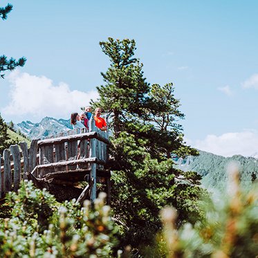 Holz-Aussichtsplattform am Zirbenweg am Graukogel, auf der mehrere Wander*innen stehen und den Blick über die umliegende Berglandschaft genießen.