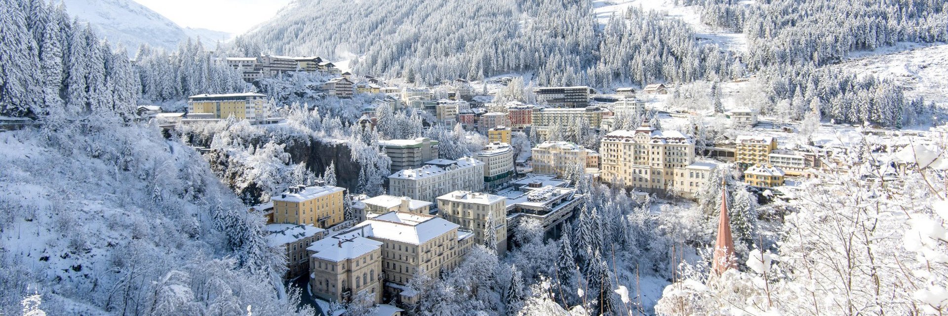 Winterliche Ansicht von Bad Gastein mit seinen markanten Belle-Époque-Gebäuden, die sich terrassenförmig an den verschneiten Berghang schmiegen; umgeben von schneebedeckten Wäldern und Bergen.