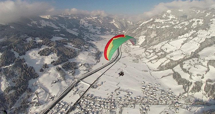 Paragleiter fliegt über das verschneite Gasteinertal mit Blick auf Dorfgastein.