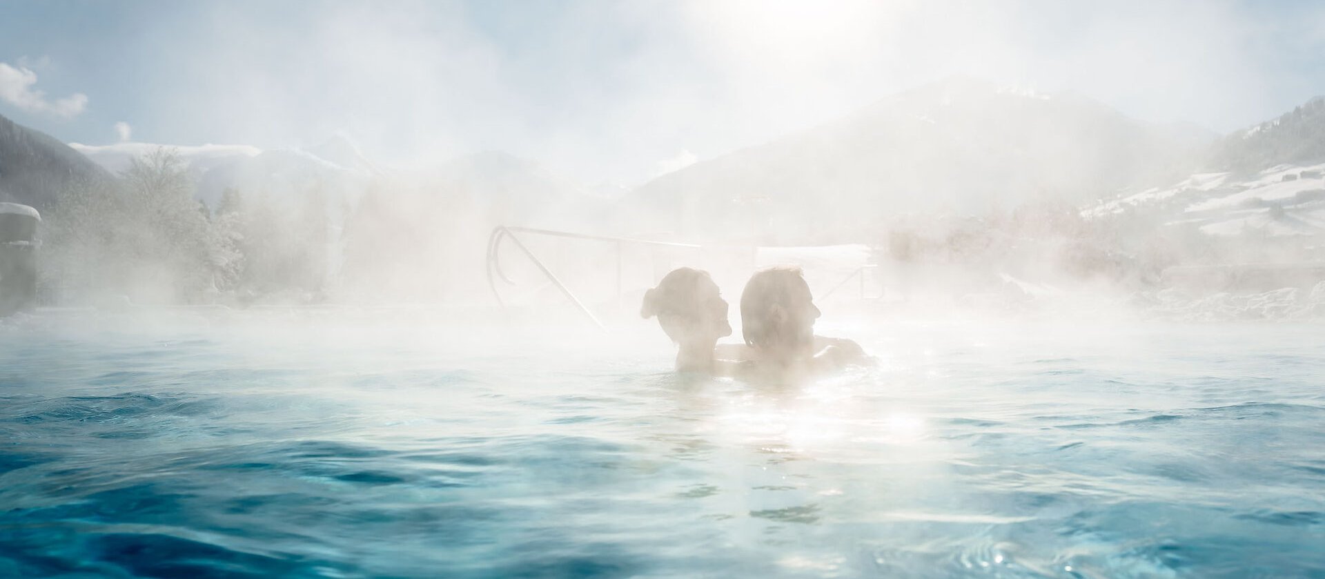 Menschen entspannen im warmen Außenbecken der Alpentherme Gastein mit Blick auf die verschneiten Berge.
