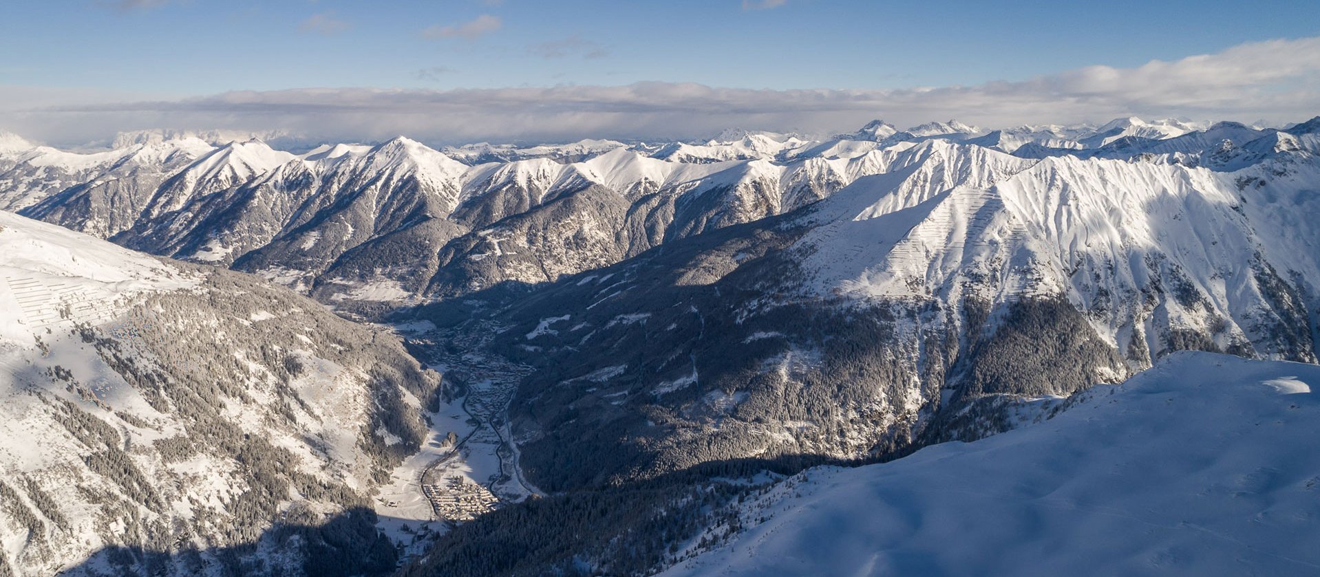Weites Panorama über das verschneite Gasteinertal mit umliegenden schneebedeckten Berggipfeln unter blauem Himmel.