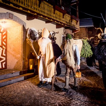 Krampus, Nikolaus und Körbelträger vor einem Haus