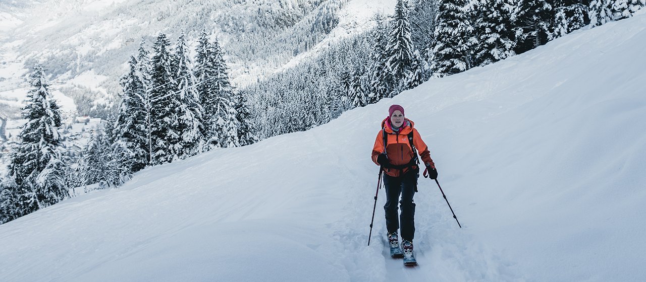 Zwei Personen unternehmen eine Skitour am Graukogel und steigen mit Tourenski durch einen verschneiten Waldhang; dichte, schneebedeckte Bäume umgeben den schmalen Aufstieg.