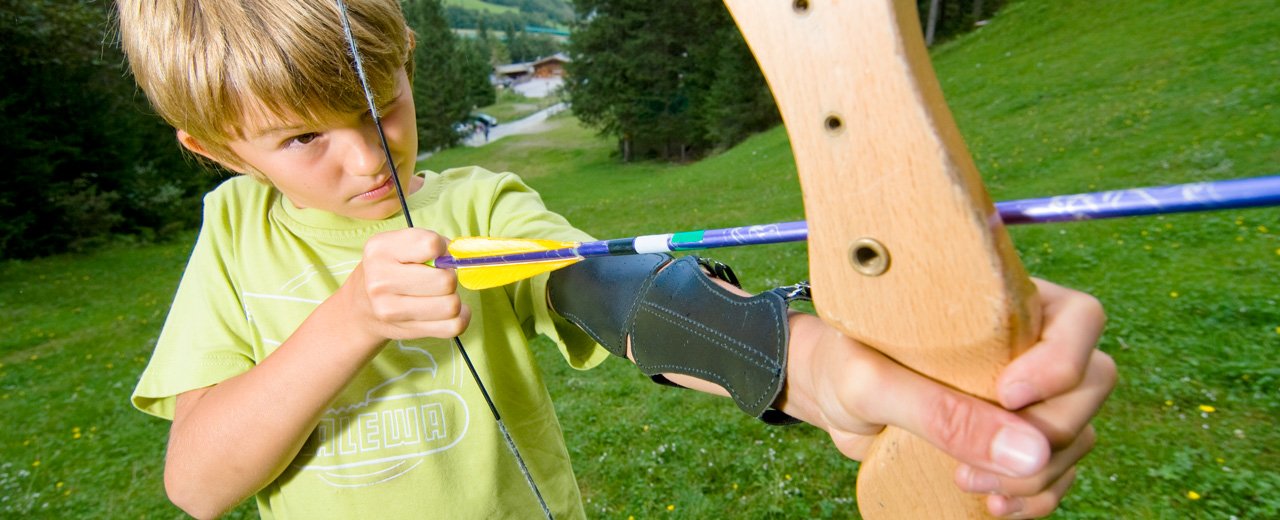 Ein Kind legt den ersten Pfeil in den Bogen. Bogenschießen in Gastein