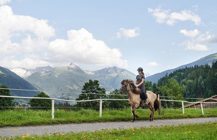 Frau reitet auf einem Pferd vor alpiner Bergkulisse im Gasteinertal.