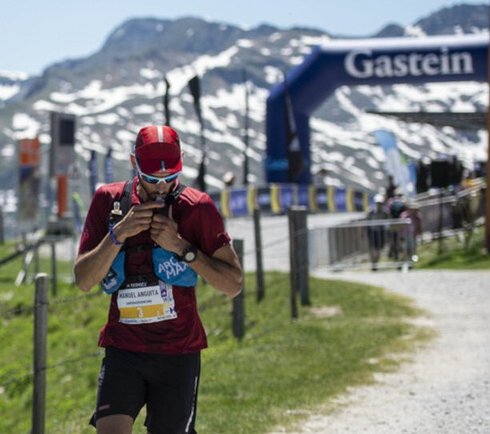 Trailrunner nahe einer Bergstation in alpiner Landschaft mit Seilbahn und schneebedeckten Gipfeln während eines Berglauf-Wettkampfs.
