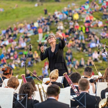 Konzert eines Orchesters bei einem Open-Air-Musikfestival in den Bergen des Gasteinertals mit Publikum auf grünen Almwiesen.