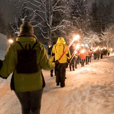 Menschen bei einer Fackelwanderung durch eine verschneite Winterlandschaft im Gasteinertal.