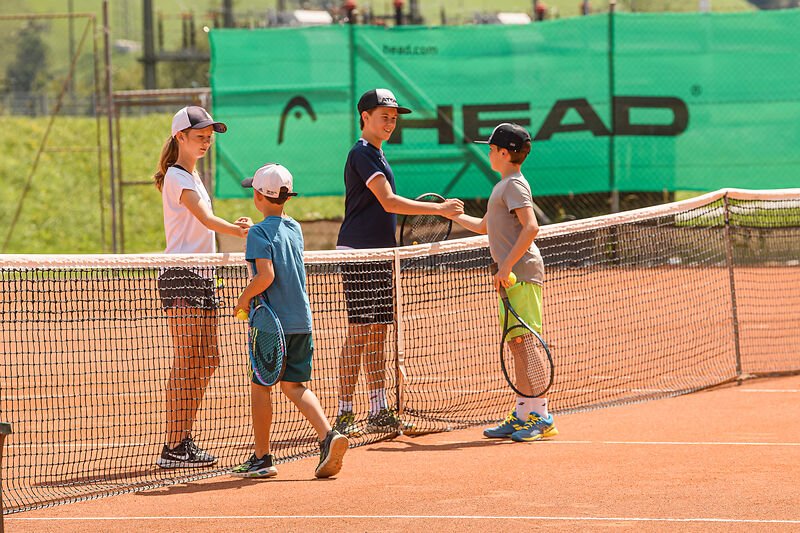 Gruppe von Kindern mit Tennisschlägern am Tennisplatz im Gasteinertal.
