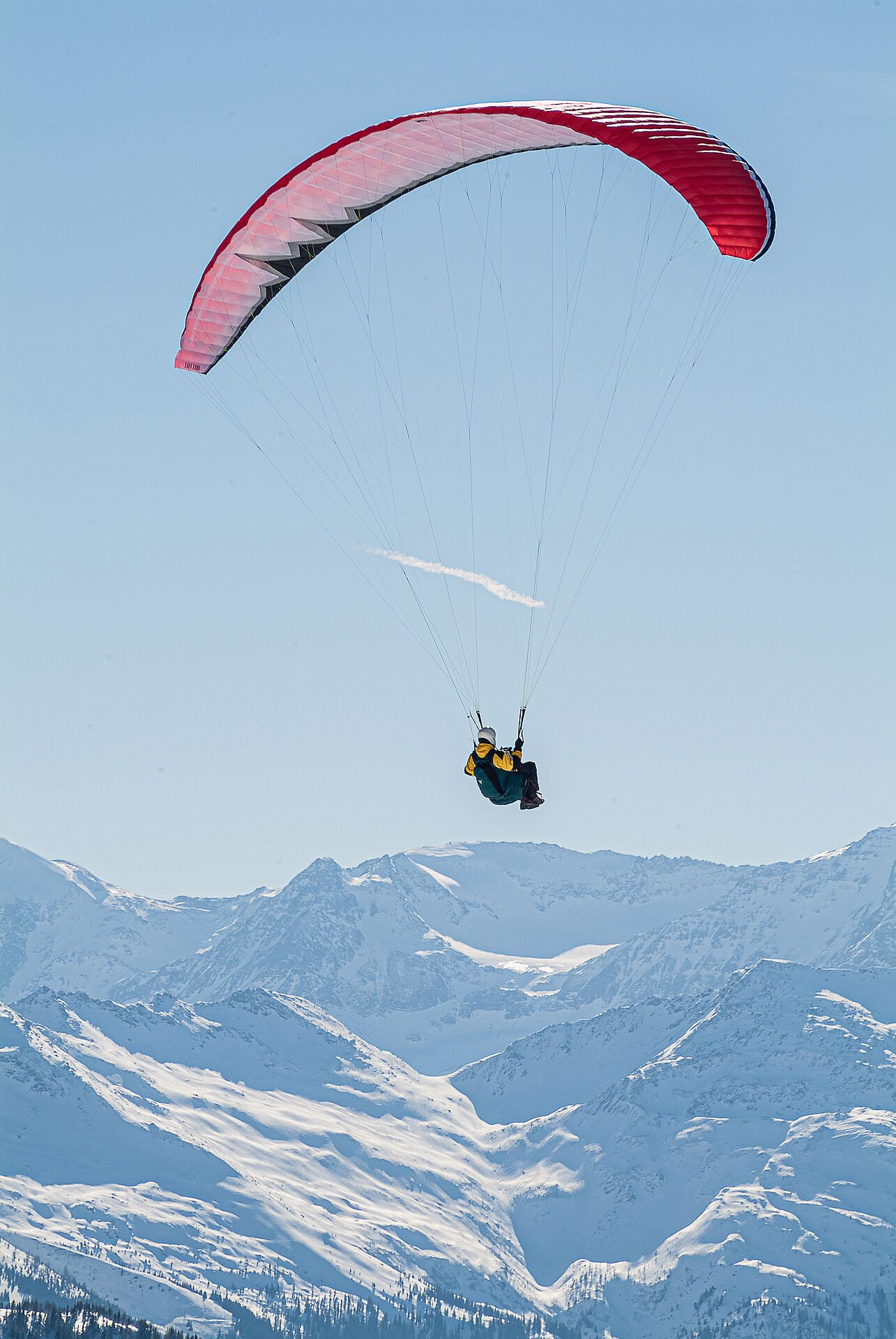 Paragleiter fliegt über verschneite Berge im Gasteinertal.