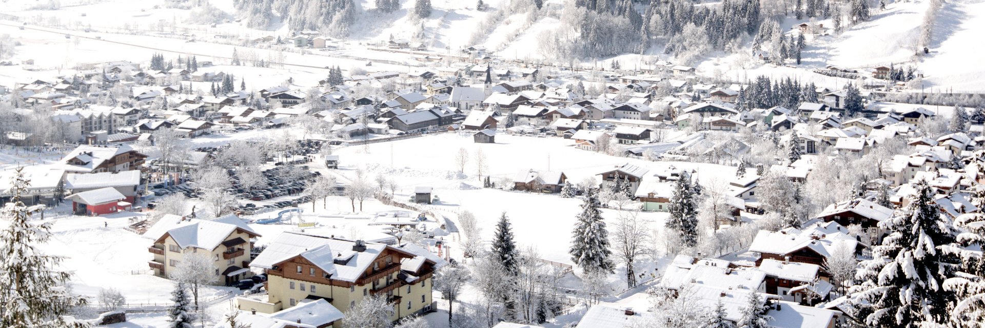 Winterliches Panorama über Dorfgastein im Gasteinertal mit verschneiten Häusern, Wiesen und Bergen im Salzburger Land.
